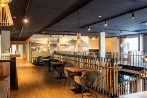 Obere Etage mit Geländer, Tischen und einem großen beleuchteten Wandgemälde einer Stadt am Wasser.