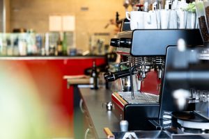 Seitenansicht einer Siebträger-Espressomaschine mit gestapelten weißen Tassen auf der Oberseite.