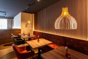 Rote und graue Sessel an Holztischen vor einer beleuchteten Lamellenwand aus Holz.