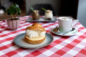 Aufgeschnittenes gefülltes Hefegebäck. Im Hintergrund stehen eine Kaffeetasse, zwei Dessertgläser und eine kleine Pflanze im Topf. Alles angerichtet auf einer rot-weiß karierten Tischdecke.