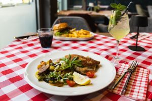 Ein paniertes Schnitzel, serviert mit gebratenen Kartoffeln, Lauch, Zucchini, Kirschtomaten und einer Zitronenspalte auf einem weißen Teller.