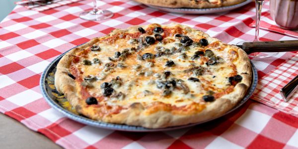 Pizza mit schwarzen Oliven auf einer rot-weiß karierten Tischdecke.