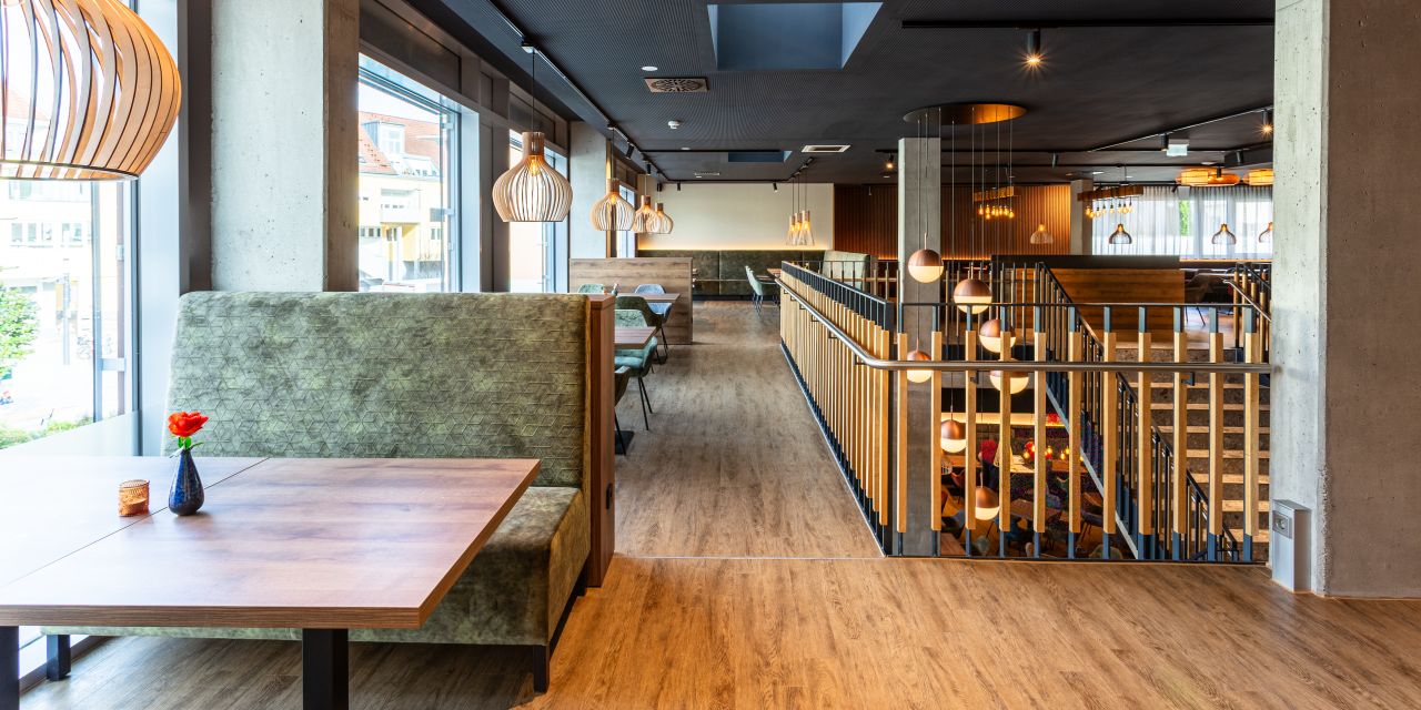 Sitzbereich mit grüner Polsterbank und großen hölzernen Lamellen-Leuchten am Treppenaufgang.