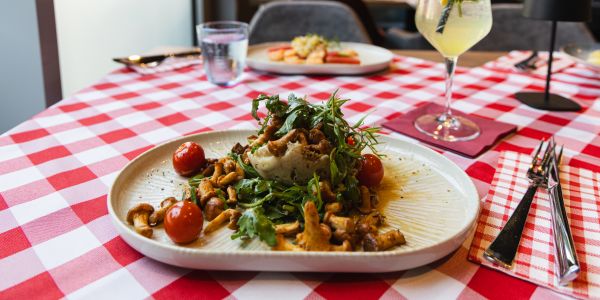 Ein Gericht mit gebratenen Pfifferlingen, Rucola und Kirschtomaten, angerichtet auf einem Püree auf einem hellen Teller.