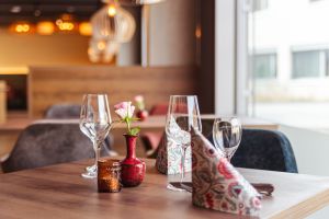 Weingläser, eine kleine Vase mit Blume und Servietten auf einer hölzernen Tischplatte.