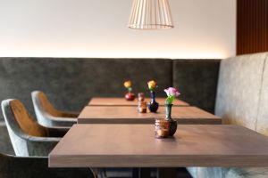 Holztische mit kleinen Vasen, einzelnen Blumen und Kerzengläsern vor einer dunklen Polsterbank.