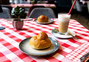 Hefegebäck und ein Latte Macchiato mit rotem Trinkhalm auf rot-weiß karierter Tischdecke.