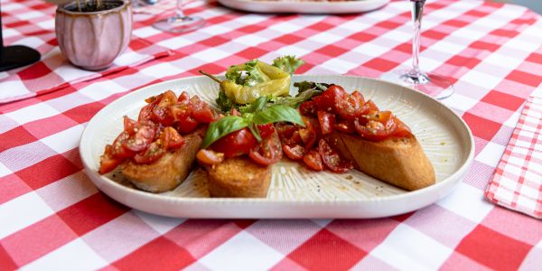 Drei geröstete Brotscheiben mit gewürfelten Tomaten und Basilikum auf einem Teller, garniert mit Salat und Peperoni.