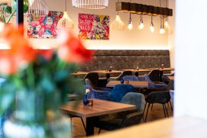 Unscharfe Blumen im Vordergrund vor einem Gastraum mit bunten Wandbildern und Hängelampen.