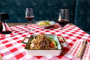 Eckige Auflaufform mit Spätzle, Röstzwiebeln und einer Kirschtomate auf rot-weiß karierter Tischdecke.