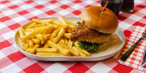Ein Burger mit knusprig paniertem Hähnchenfleisch und eine Portion Pommes frites auf einem hellen Teller.