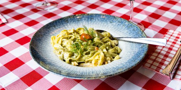 Teller mit Pasta an grüner Sauce, mit Kirschtomate und Dill auf einer rot-weiß karierten Tischdecke.