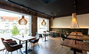 Tische mit farbigen Polstersesseln vor einer bodentiefen Fensterfront.